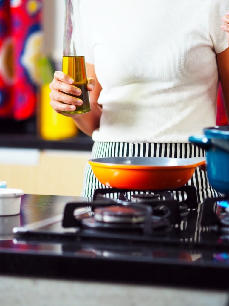 person holding bottle of oil at gas stove